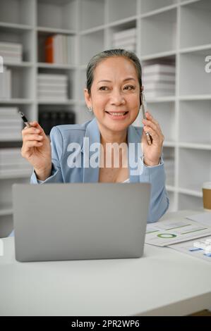 Attraktive und glückliche Geschäftsfrau, die mit ihrem Geschäftspartner am Schreibtisch telefoniert. Stockfoto