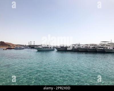 Eine Vielzahl von Motor- und Segelschiffen, Booten und Kreuzfahrtschiffen stehen an einem Dock im Hafen vor dem Hintergrund des blauen Meeres und des Berges aus braunem Stein Stockfoto