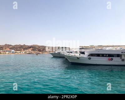 Eine Vielzahl von Motor- und Segelschiffen, Booten und Kreuzfahrtschiffen stehen an einem Dock im Hafen vor dem Hintergrund des blauen Meeres und des Berges aus braunem Stein Stockfoto