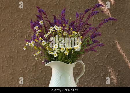 Wunderschöner Blumenstrauß mit Feldblumen im Krug nahe der braunen Wand Stockfoto