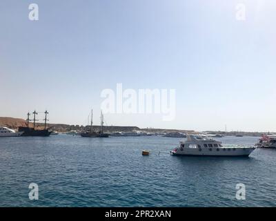 Eine Vielzahl von Motor- und Segelschiffen, Booten und Kreuzfahrtschiffen stehen an einem Dock im Hafen vor dem Hintergrund des blauen Meeres und des Berges aus braunem Stein Stockfoto