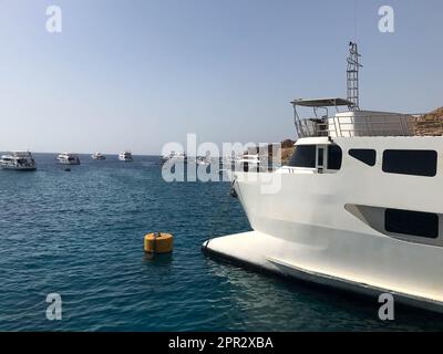 Eine Vielzahl von Motor- und Segelschiffen, Booten und Kreuzfahrtschiffen stehen an einem Dock im Hafen vor dem Hintergrund des blauen Meeres und des Berges aus braunem Stein Stockfoto