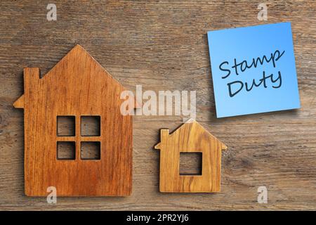 Hausfiguren und Haftnotiz mit Text Stamp Duty auf Holzhintergrund, flach liegend Stockfoto