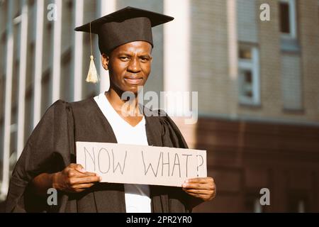 Porträt eines verärgerten afroamerikanischen Mannes, der mit einem Pappposter auf der Straße neben dem Gebäude auf der Suche nach einem Job stand. Universitäts- oder Hochschulabschluss Stockfoto