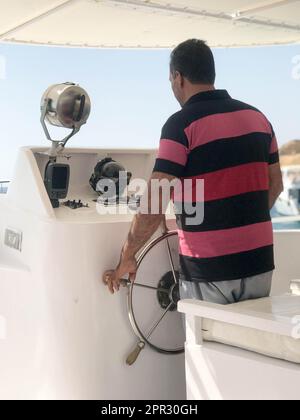 Ein fauler Kapitän, ein Araber in einem rot gestreiften Hemd, kontrolliert ein Schiff, ein Boot am Ruder des Meeres. Stockfoto