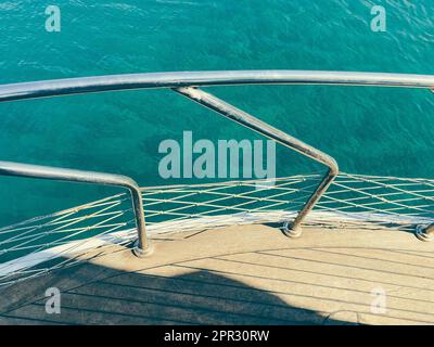 yacht auf dem offenen Meer. Meer mit Sandstrand vor dem Hintergrund eines Berges. Die Yacht hat ein Holzbrett mit Metallgeländern. Stockfoto