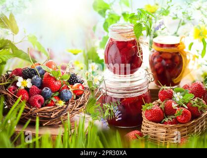 Frische Sommerbeeren in Körben und hausgemachte Marmelade in Gläsern Stockfoto