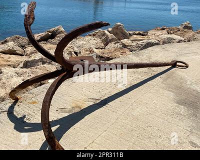 Der letzte Teil eines alten rostigen Ankerplatzes, der auf einem Steinhintergrund als Souvenir für Touristen platziert wurde Stockfoto