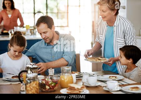 Das Frühstück wird immer mit einer guten Hilfe von Liebe serviert. Eine Familie mehrerer Generationen, die zusammen zu Hause frühstückt. Stockfoto