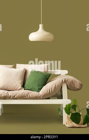 Gemütliches Sofa mit Kissen, Lampe und Zimmerpflanzen auf grünem Hintergrund Stockfoto