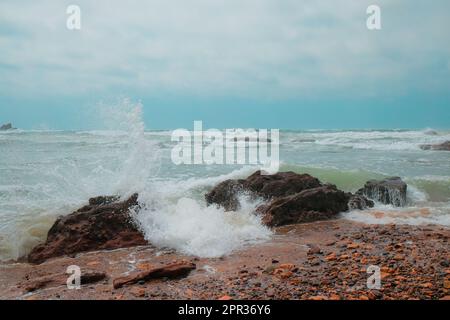 Am Strand von Legzira Beach stürzen die Wellen gegen Felsen. Zerklüftete Küste in der marokkanischen Provinz Tiznit. Raue Wellen im Atlantischen Ozean. Seascape. Stockfoto