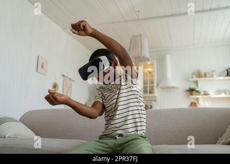 Der konzentrierte, zufriedene Schwarze spielt Videospiel-Rennen und fährt das Auto in einer Virtual-Reality-Brille. Stockfoto