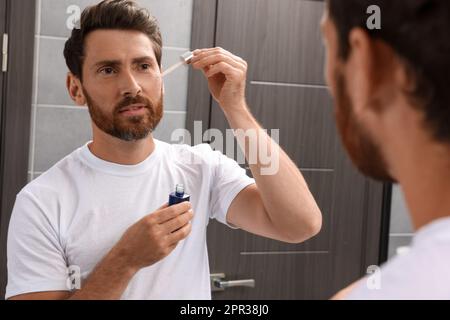 Ein gutaussehender Mann, der im Bad Öl auf den Bart aufträgt Stockfoto
