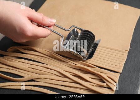 Frau schneidet Teig für Soba am Tisch, Nahaufnahme Stockfoto