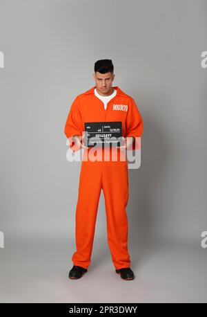 Gefangener in orangefarbenem Overall mit Fahndungsbrieftafel auf grauem Hintergrund Stockfoto
