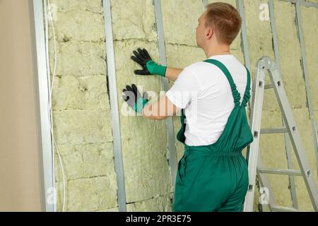 Arbeiter, der Wärmedämmmaterial an der Wand in Innenräumen installiert Stockfoto