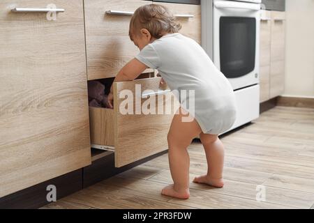 Kleines Kind, das die Schublade in der Küche erkundet. Gefährliche Situation Stockfoto