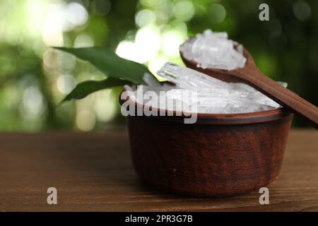 Schüssel und Löffel mit Menthol-Kristallen auf einem Holztisch vor verschwommenem Hintergrund Stockfoto