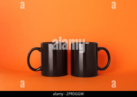 Leere schwarze Keramikbecher auf orangefarbenem Hintergrund Stockfoto
