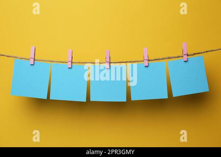Holzkleidekabinen mit leeren Notizzetteln auf Garn vor gelbem Hintergrund. Platz für Text Stockfoto