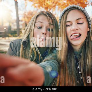 Freunde sind die Leute, mit denen man verrückt sein kann. Zwei junge Freunde ziehen lustige Gesichter, während sie draußen für ein Selfie posieren. Stockfoto