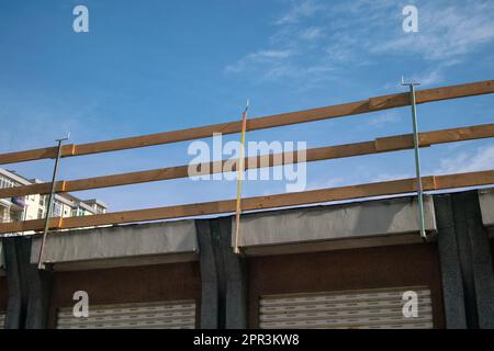 Fallschutzgerüst auf einer Baustelle. Dach mit Holzgeländern an der Dachkante, die an den Dachtrassen des Gebäudes eingehakt sind. Stockfoto