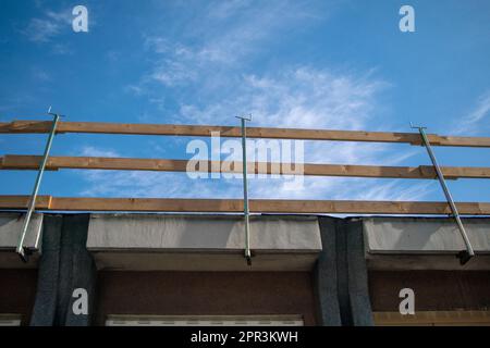 Fallschutzgerüst auf einer Baustelle. Dach mit Holzgeländern an der Dachkante, die an den Dachtrassen des Gebäudes eingehakt sind. Stockfoto