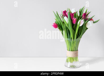 Farbenfrohe Frühlingstulpen in einer Vase auf einem weißen Tisch. Modell zur Ausstellung von Werken. Vase mit Tulpen auf weißem Hintergrund, Platz für Ihren Text. Stockfoto