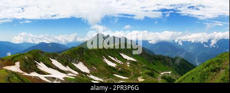 Atemberaubende Berglandschaft an sonnigen Sommertagen. Berge mit grünem Gras bedeckt mit Schnee vor einem bewölkten Himmel im Kaukasus Hochland. Stockfoto