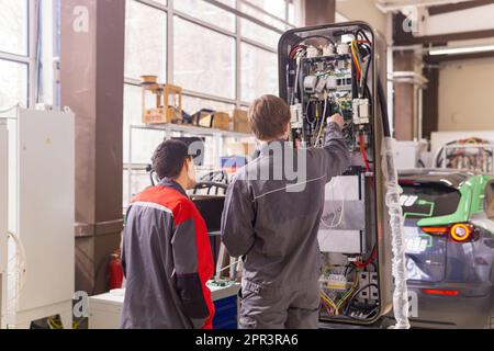 Perm, Russland - 25. April 2023: Arbeiter, die Ladestationen für Elektrofahrzeuge in der Werkstatt montieren Stockfoto