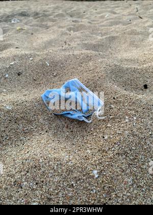 Einweg-medizinische Gesichtsmaske sind an einem Strand, bedeckt mit Sand, was zu schlechten Folgen führt. Umweltverschmutzungskonzept Stockfoto