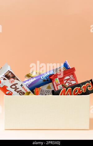 Arahal. Sevilla. Spanien. 18. März 2023. Geschenkbox mit verschiedenen Schokoladen und Pralinen bekannter Marken auf hellorangefarbenem Hintergrund. Stockfoto