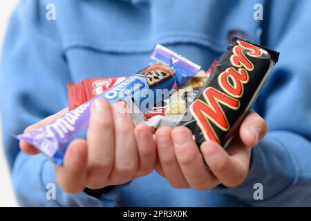 Arahal. Sevilla. Spanien. 18. März 2023. Hände eines Kindes mit Schokolade verschiedener Marken. Ein übermäßiger Zuckerkonsum kann negative CO-Emissionen zur Folge haben Stockfoto