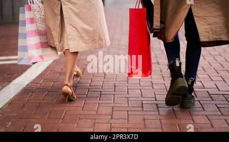Rückansicht von zwei unbekannten Frauen, die draußen mit Einkaufstaschen herumlaufen. Stockfoto