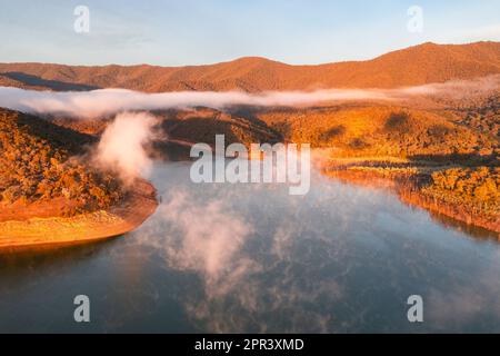 Der Nebel über einem See, umgeben von Bergen im frühen Morgenlicht über dem Lake Eildon in Victoria, Australien, aus der Vogelperspektive Stockfoto