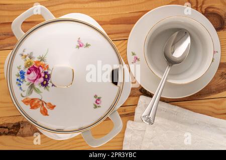 Eine alte Porzellanröhre, Suppenteller und Metalllöffel auf einem Holztisch, Makro, Draufsicht. Stockfoto
