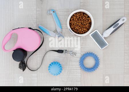 Die rosafarbene einziehbare Hundeleine, der Nagelschneider, der Haarkamm, Lebensmittel und Spielzeuge liegen auf dem Boden Stockfoto