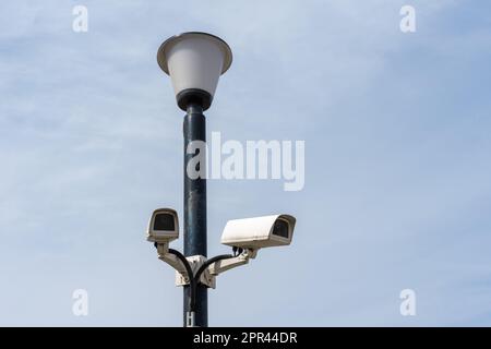 Überwachungskameras, die an einem Lampenpfosten vor einem blauen Himmel befestigt sind. Überwachungskamera. Sicherheit in der Stadt. Versteckte Filmaufnahmen von dem, was passiert. Stockfoto