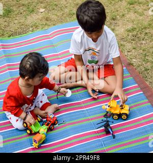 Zwei glückliche Jungs im Gesellschaftspark, glückliche asiatische Brüder, die glücklich zusammen lächeln. Brüder spielen im Sommer draußen, beste Freunde. Kleinkind Baby bo Stockfoto