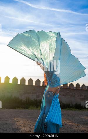 Orientalische Tänzerin in Blau mit Isis-Flügeln der gleichen Farbe, die bei Sonnenuntergang auf einem arabischen Denkmal tanzt Stockfoto