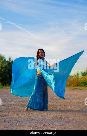 Orientalische Tänzerin in Blau mit Isis-Flügeln der gleichen Farbe, die draußen tanzt Stockfoto