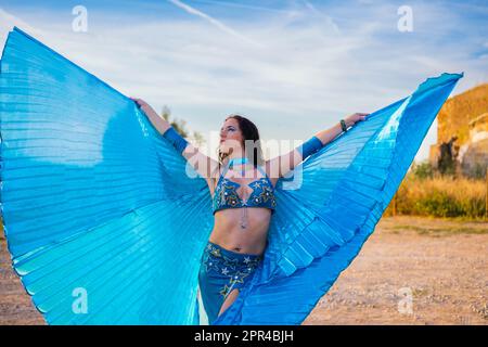 Orientalische Tänzerin in Blau mit Isis-Flügeln der gleichen Farbe, die draußen tanzt Stockfoto