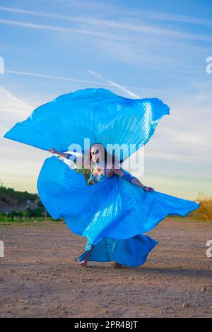 Orientalische Tänzerin in Blau mit Isis-Flügeln der gleichen Farbe, die draußen tanzt Stockfoto