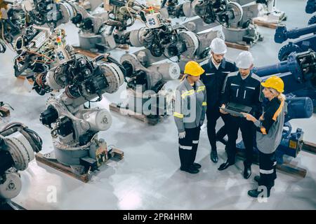 Ingenieurteam Diversity arbeitet in einer modernen Industrie-Robotik-Fabrik zusammen. Ingenieure arbeiten bei der Maschinenmontage um den Roboterarm herum zusammen Stockfoto