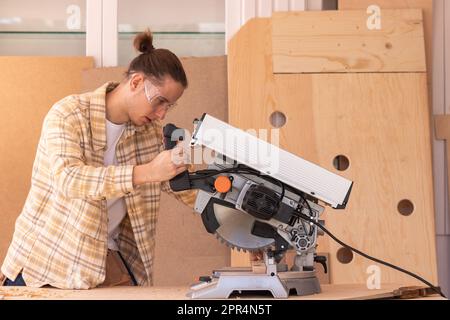 Seitenansicht eines konzentrierten Werkers, der Holzblock mit Kreissäge in der Werkstatt sägt Stockfoto