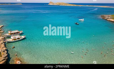Blick aus der Vogelperspektive auf Touristenboote und Schwimmer im kristallklaren Wasser vor einem kleinen Strand (Kolokitha, Kreta, Griechenland) Stockfoto