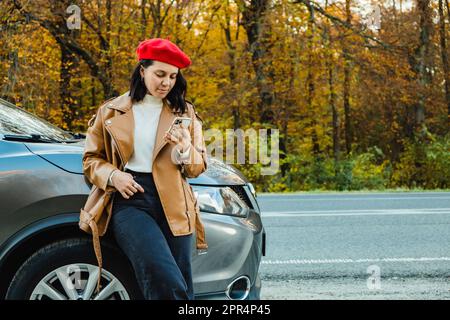 Die Frau mit der roten Baskenmütze überprüft ihr Handy bei einem geparkten Auto Stockfoto