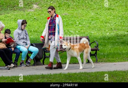 Ein Mädchen geht mit ihrem Hund im Park spazieren. Eine ältere Frau sitzt mit ihren Enkeln auf einer Bank und liest ein Buch. 23. April 2023, Belarus Stockfoto