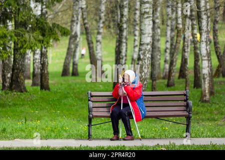 Eine ältere Frau ist müde und schläft auf einer Bank in einem Quellpark. Stockfoto