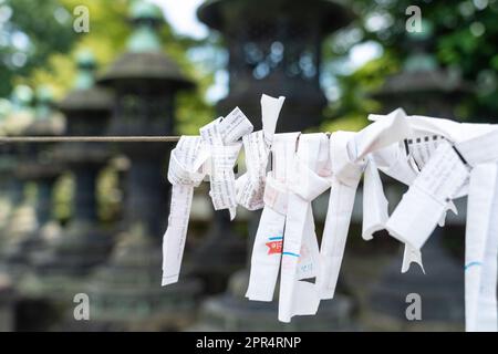 Japanische Omikuji-Glückssträhnen, die beim Ueno Tosho-gu-Schrein Honden und Karamon im Ueno Park, Tokio, Japan, an ein Seil gebunden sind. Omikuji, die auf Pech hindeuten, sind an die Schnur gebunden, um das Pech loszuwerden. Stockfoto